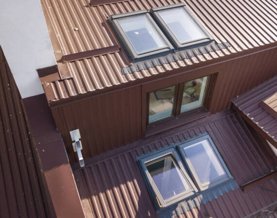 Aerial view of annex room exterior with plastic attic windows, roof and walls covered with brown metal decorative siding planks.