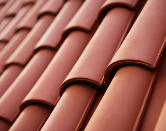 Red ceramic roof tiles covering residential building roof. Tile pattern close-up