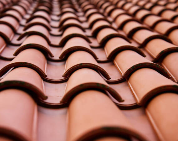 Red ceramic roof tiles covering residential building roof. Tile pattern close-up